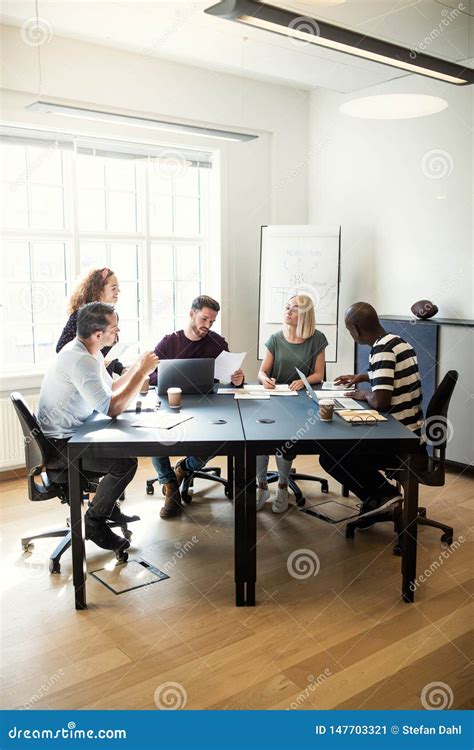 Group Of Diverse Designers Talking Together Around An Office Tab Stock