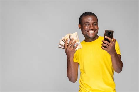 Premium Photo Excited Young Black Man Holding Money And Using His Phone