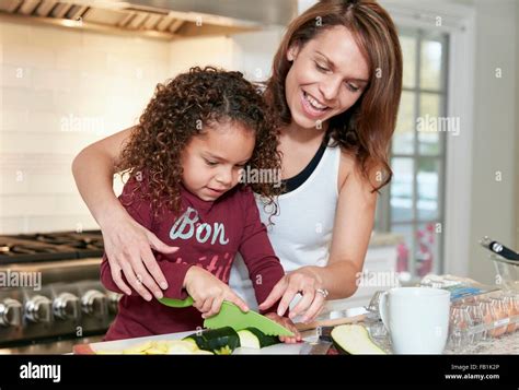 Mother Helping Daughter Chop Vegetables In Kitchen Stock Photo Alamy