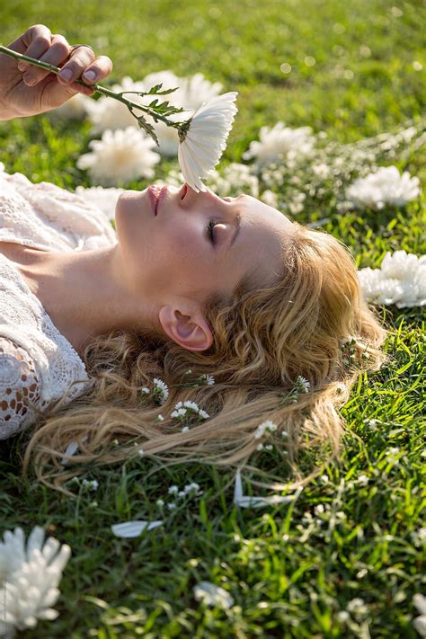 Beautiful Blonde Woman Lying On Green Grass And Smelling White Flowers