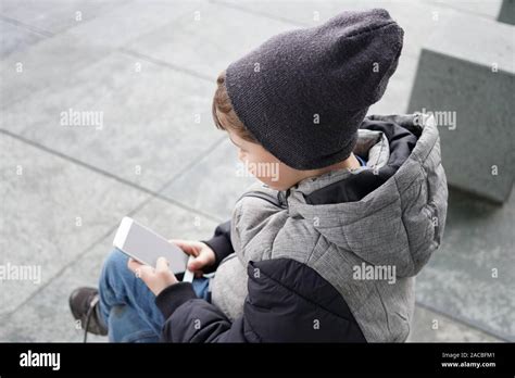 7 Year Old Boy Looking At Smartphone Mobile Cell Phone Sitting Outside