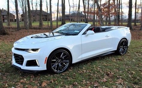 A White Chevrolet Camaro Is Parked In The Grass Near Some Trees And