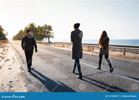Group Of People Walk Along The Road At The Seaside Three Young Stock