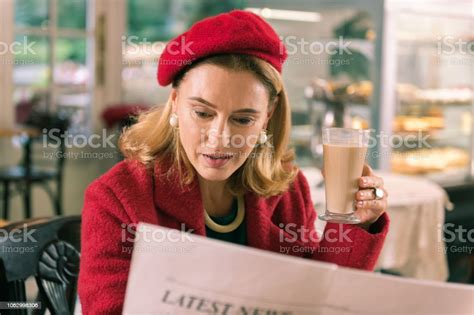 Mature French Woman Reading Morning Newspaper Sitting In Bakery Stock
