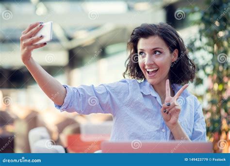 Portrait Of A Playful Young Girl Taking Selfie With Mobile Phone While Sitting With Laptop