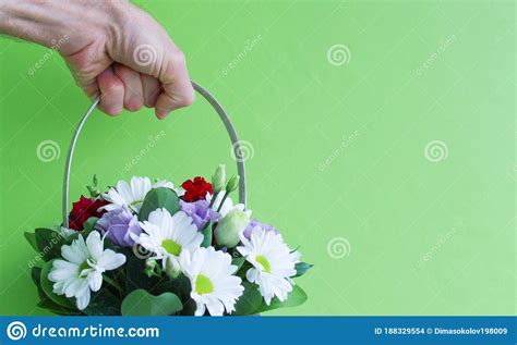 A Hand Holds Colorful Flowers In A Basket Isolated On A Green
