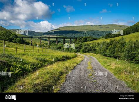 Road Up Glen Auch In Scottish Highlands With Train Viaduct On The