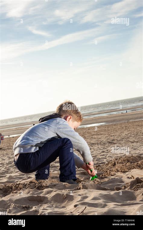 A Young Caucasian Boy Digging A Hole In The Sand At Formby Beach