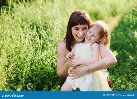 Happy Beatiful Mom Kisses And Hugs Daughter On Nature In Sunset Light