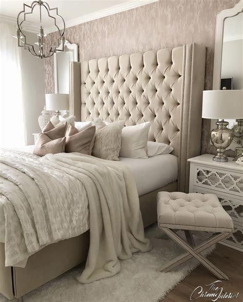 A bright feminine bedroom with a cnaopy bed, a wooden bench and a woven chair, a statement plant and a floral chandelier. 20 Feminine Master Bedrooms - The Marble Home