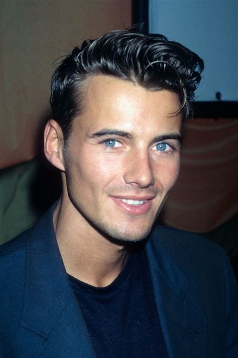 A Man In A Suit Smiling At The Camera With Blue Eyes And Black Hair On