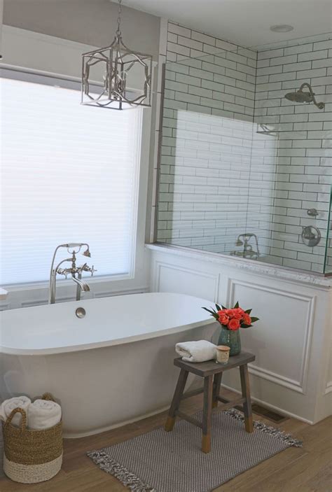 A White Bath Tub Sitting Under A Window Next To A Wooden Table With