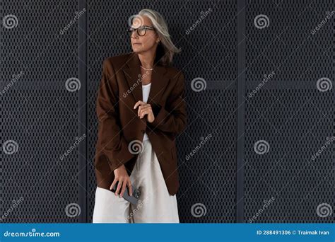 a slender gray haired mature business lady dressed in a stylish jacket walks along the city