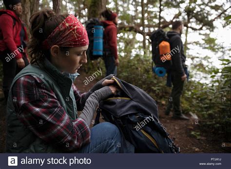 Woman Backpacking In Woods With Friends Looking In Backpack Stock
