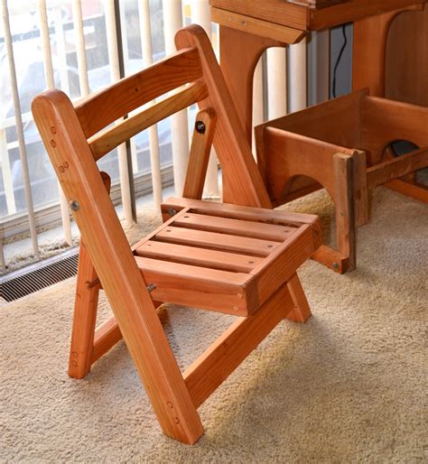 Kid's Wooden Folding Chair A wooden seating group, consisting of a wooden table, wooden chairs and a wooden bench in front of a house wall, chained against theft and covered with a green layer of algae, moss and lichen, just like the paved floor.