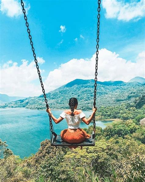 A Woman Is Sitting On A Swing Overlooking The Water