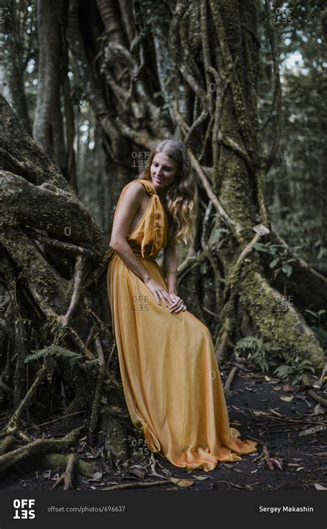 Blonde Woman Wearing Golden Dress Leaning On A Banyan Tree Stock Photo