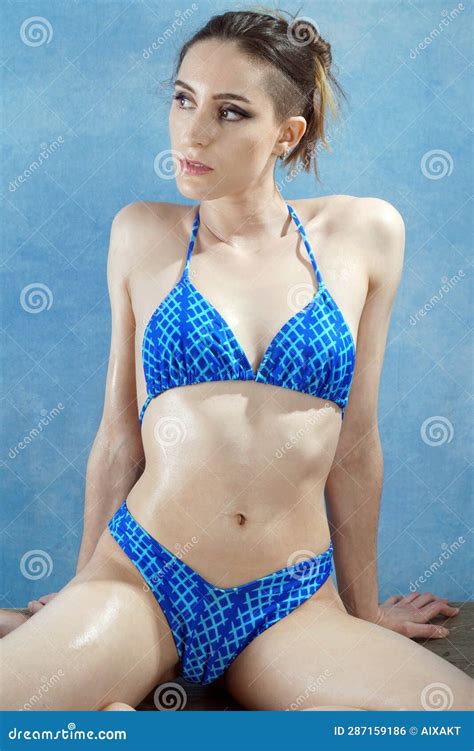 Beautiful Wet Oiled Woman Sitting In Blue Bikini In Studio Stock Photo