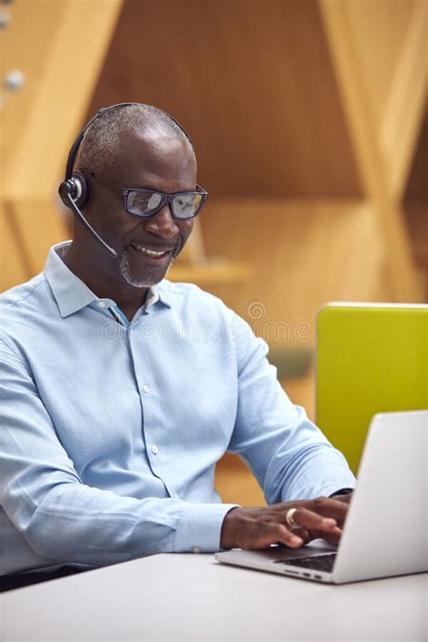 Mature Businessman Wearing Phone Headset Talking To Caller In Busy