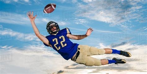 Male Teenage American Football Player Reaching To Catch Ball Mid Air