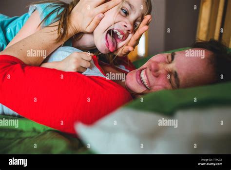 Side View Of Playful Daughter Licking Mother Lying On Bed At Home Stock