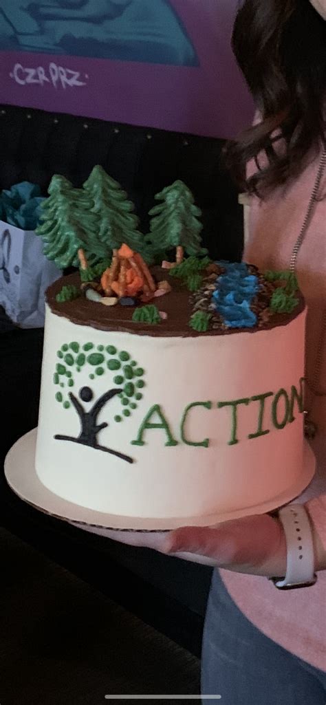 A Woman Holding Up A Cake With Trees On The Top And Action Written On It
