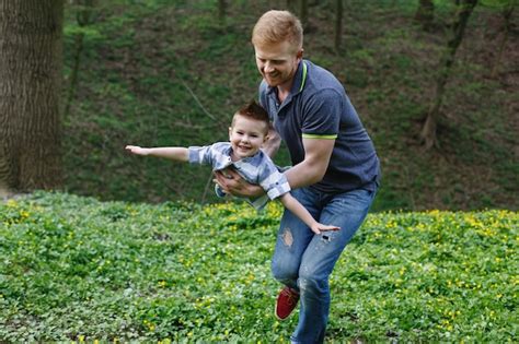 Papá Gira A Su Hijo Como Un Avión Jugando En El Parque Verde Foto Gratis