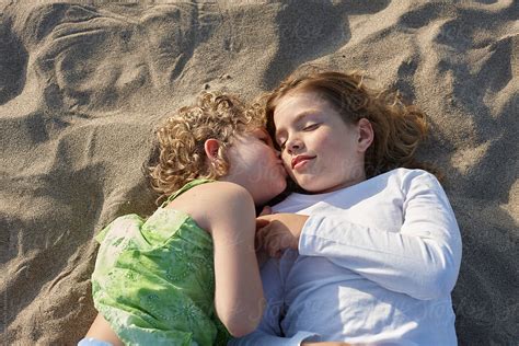 Two Sisters Lying On The Beach Kissing On The Cheek By Stocksy Contributor Miquel Llonch