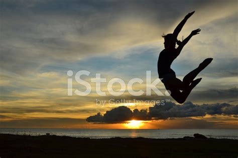 Girl Doing Gymnastics Jump At The Beach During Sunset Stock Photo