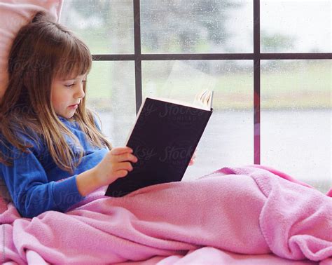 A Young Girl Sits In A Window Seat Reading A Book On A Rainy Day By Stocksy Contributor Tana