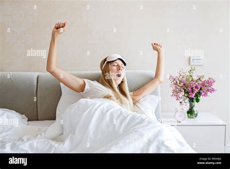 Happy Young Blonde Woman In Pajamas And Blindfold Waking Up Yawning