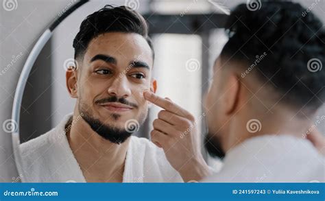 Arabian Indian Arab Hispanic Millennial 30s Bearded Man Applying Moisturizer Cream On Face Skin
