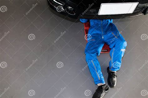 Mechanic In Blue Uniform Lying Down And Working Under Car At The Stock