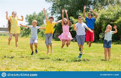 Happy School Children Jumping On The Green Lawn In Park Stock Image