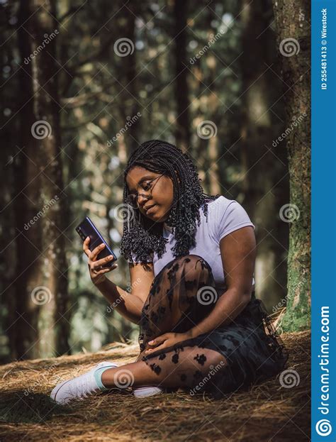 African American Woman Sitting On The Grass In A Forest Using Her