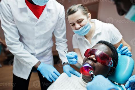 Multiracial dentist doctors team. African american man patient at UV