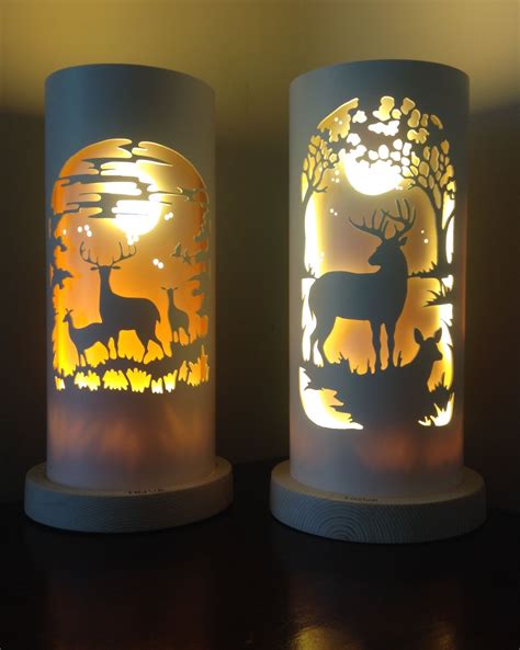 Two Lamps With Deer And Trees On Them Sitting On A Table Next To Each Other