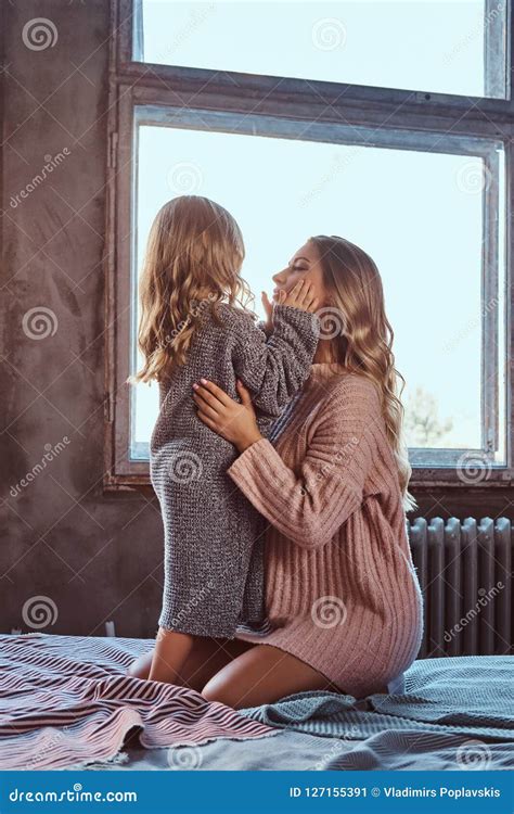 Mom And Her Daughter Cuddling Together While Sitting On Bed In Winter Evening Stock Image