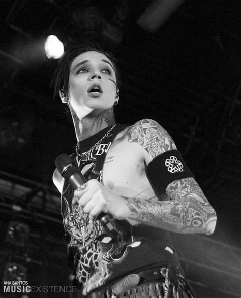 A Man With Tattoos On His Arm Holding A Microphone And Looking Up At