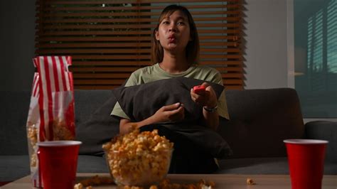 mulher jovem animada comendo pipoca e assistindo televisão no sofá passando seu tempo livre em