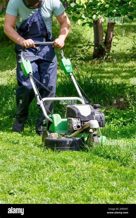 A Gardener Mows Green Grass With An Industrial Gasoline Mower Tends A