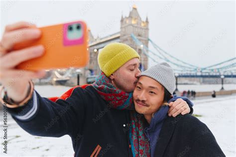 Young Happy Asian And Caucasian Same Sex Interracial Couple Kissing And Laughing Taking A Selfie