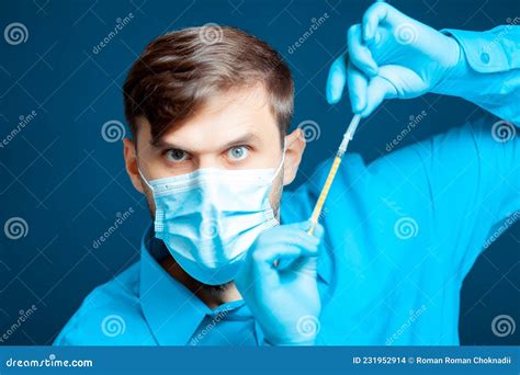 a doctor in a medical mask and gloves in a blue uniform is holding a thin syringe for