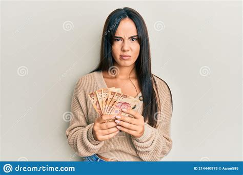 Young Beautiful Hispanic Girl Holding Mexican Pesos Skeptic And Nervous