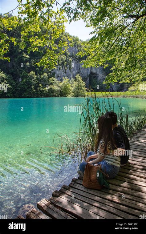 Couple Sits On Wooden Plank Path And Admires Clear Water In A Pool