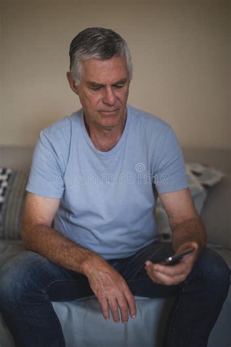 Upset Senior Man Holding Mobile Phone While Sitting On Sofa Stock Image