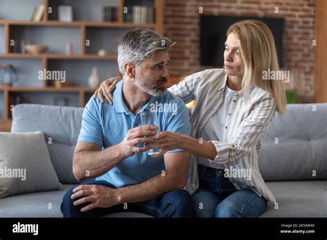 Sad Middle Aged European Wife Gives Water And Calms Depressed Unhappy Man In Living Room