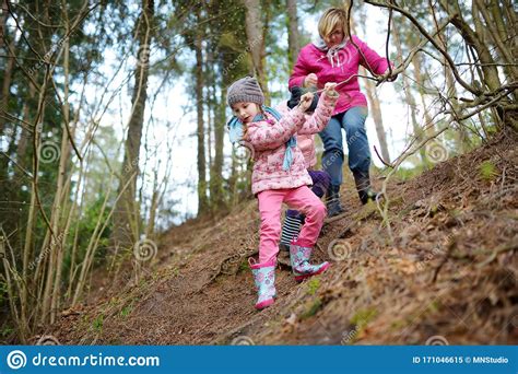 Two Cute Little Sisters Hiking In A Forest With Their Grandmother On