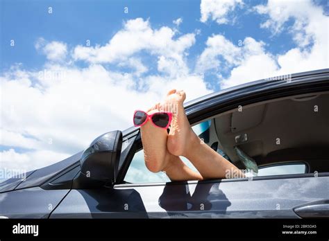 Close Up Of Sunglasses Over The Womans Feet Out Of Car Window Against