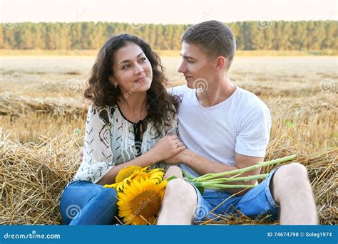 Happy Young Couple Sit In Wheaten Field At Evening Romantic People